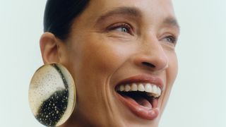 An image of a smiling woman with her hair slicked back into an updo and wearing big circular gold earrings